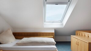 Ein Schlafzimmer mit Oberlichter, einem Bett, einer hölzernen Kommode und einem kleinen Schreibtisch.