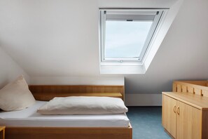 Une chambre avec un puits de lumière, un lit, une commode en bois et un petit bureau.