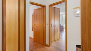 Un couloir avec des portes en bois qui donnent sur une pièce où l’on aperçoit un coin cuisine au fond.