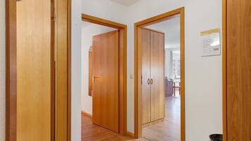 Ein Korridor mit Holztüren, die zu einem Raum führen, im Hintergrund ist eine Küche erkennbar.