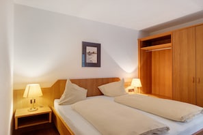 A bedroom with a wooden headboard, two bedside tables with lamps, a bed with white bedding, and a wooden wardrobe.
