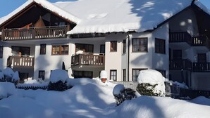 Un chalet à plusieurs étages, doté de balcons, entouré d’un paysage enneigé et d’arbres.