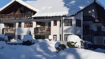 Ein mehrstöckiges Chalet mit Balkonen, umgeben von verschneitem Gelände und Bäumen.