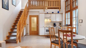 A modern kitchen with white cabinets, a wooden staircase, and a dining area with wooden chairs and a table.