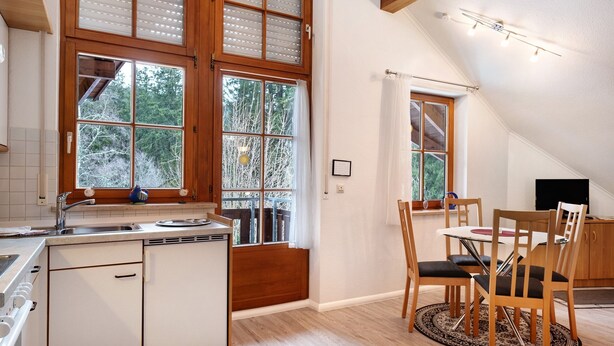 A kitchen with a dishwasher, a dining table with chairs, and a window with a view of trees.