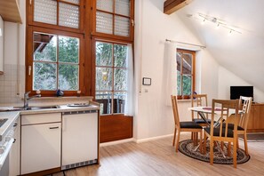 Een keuken met een vaatwasser, een eettafel met stoelen en een raam met uitzicht op bomen.