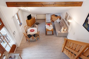 Un salon chaleureux avec un plafond en bois, un canapé, une table à manger avec des chaises et un téléviseur.