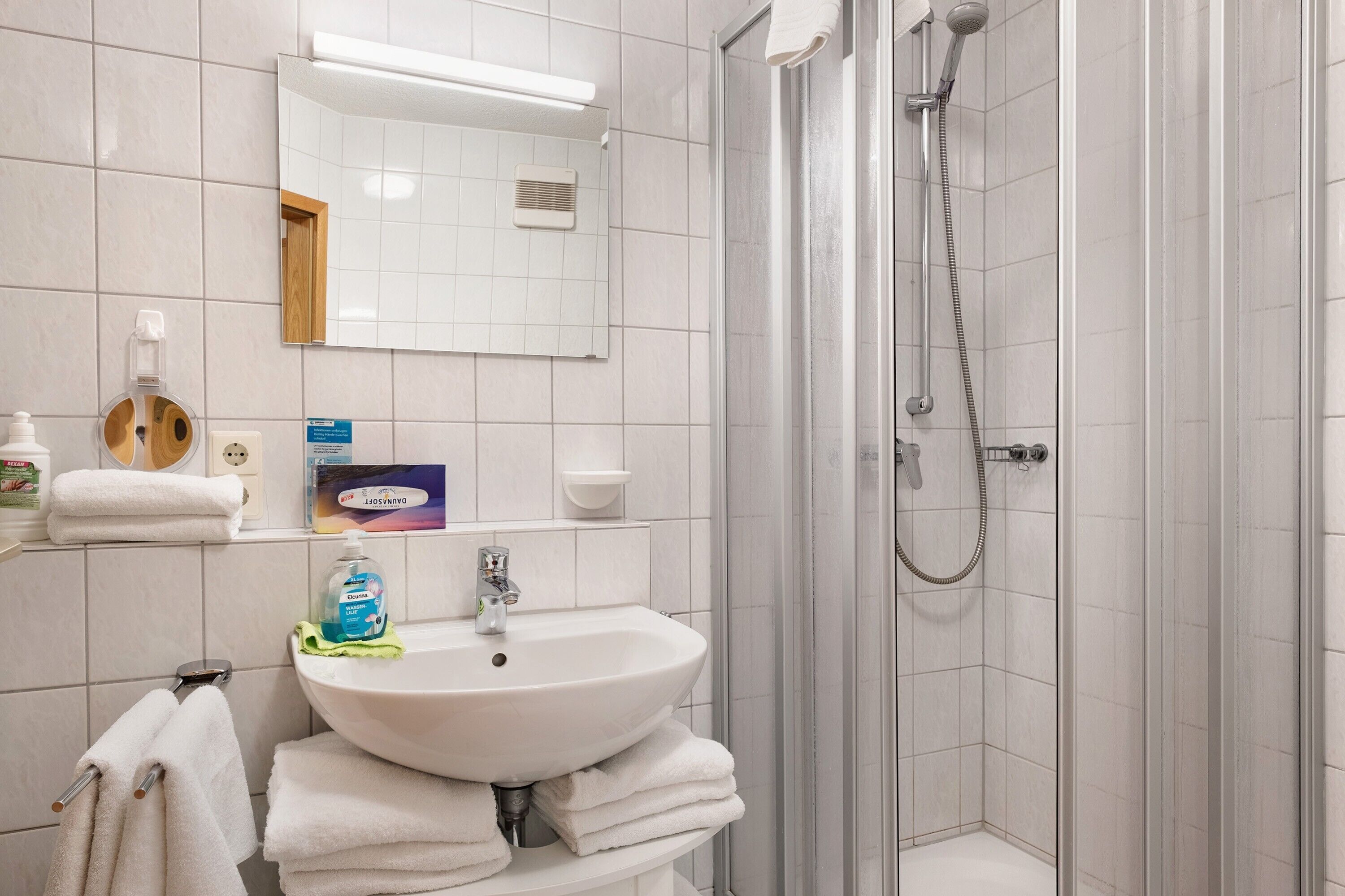 A bathroom with a sink, mirror, shower, and stacked towels.