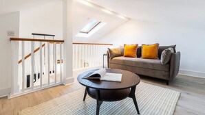 A modern living room with a sofa, a coffee table, and a staircase with a railing. - Stylish Chelsea Flat with Luxe Comfort & Charm (London)