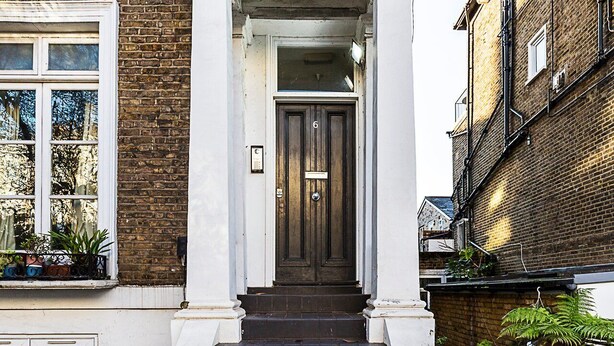 A traditional brick house with a dark wooden front door, white columns, and a small window with plants. - Stylish Chelsea Flat with Luxe Comfort & Charm (London)