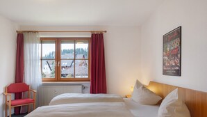 Une chambre d’hôtel avec un lit, une chaise, une fenêtre avec des rideaux et un tableau accroché au mur.