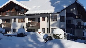 Un chalet à plusieurs étages, doté de balcons, entouré d’un paysage enneigé et d’arbres.