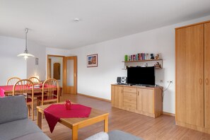 Uma sala de estar com sofá, uma mesa de jantar com cadeiras, uma cozinha com televisão e um guarda-roupa de madeira.