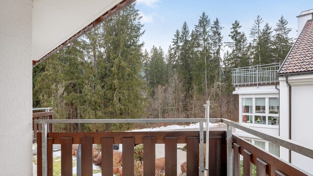 Un balcon doté d’une balustrade en bois, donnant sur un jardin agrémenté de plantes en pot et d’arbres.