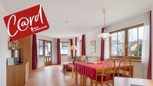Une pièce spacieuse comprenant une table à manger, des chaises, un canapé, un téléviseur et une fenêtre avec des rideaux.