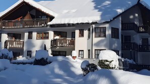 Ein mehrstöckiges Chalet mit Balkonen, umgeben von verschneitem Gelände und Bäumen.