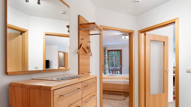 Ein modernes Schlafzimmer mit einer Holzkommode, einem großen Spiegel und einer Schiebetür, die auf einen Balkon führt.