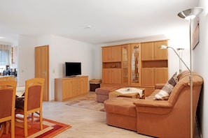 Un salon comprenant un canapé, un téléviseur, des meubles en bois, une table à manger avec des chaises et un lampadaire.