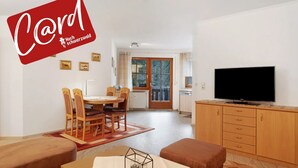 Ein modernes Wohnzimmer mit Essbereich, einem Fernseher und einer Küche im Hintergrund.