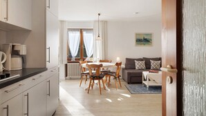 Une cuisine moderne avec des meubles blancs, un coin repas avec des chaises en bois, un canapé et un tableau au mur.