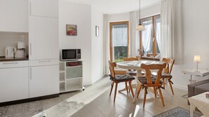 Une cuisine moderne avec des meubles blancs, un coin repas avec une table ronde et des chaises en bois, et un petit coin salon avec un canapé et une lampe.