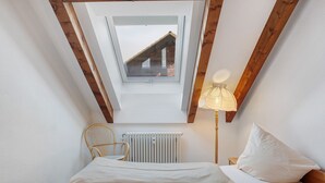 A bedroom with a skylight, a bed, a chair, a lamp, and a radiator.