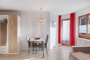 Une pièce moderne comprenant une table à manger, des chaises, un canapé, un radiateur et une fenêtre avec des rideaux rouges.