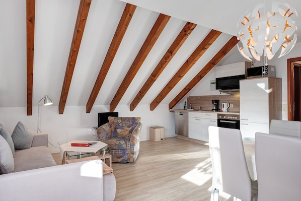 Un loft moderne avec des poutres apparentes, un coin repas, un canapé et une cuisine équipée d’un téléviseur.