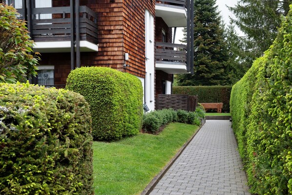 A pathway leading to a building with a wooden facade and a balcony.