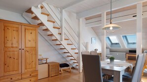 Un intérieur moderne avec un escalier en bois, un coin repas comprenant une table et des chaises, et une grande armoire en bois.