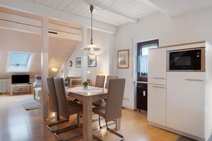 A modern kitchen with a built-in microwave, a dining area with a table and chairs, and a visible ceiling with wooden beams.