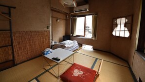 Una habitación japonesa tradicional con suelo de tatami, un futón, una mesita con un control remoto y una ventana con vistas al exterior.