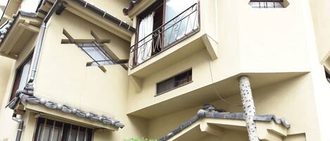 A multi-story building with a traditional architectural style, featuring a balcony on the second floor and a stone pathway leading to the entrance.