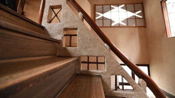 Una escalera de madera con barandilla que lleva a una habitación con un ventanal de diseño geom étrico.