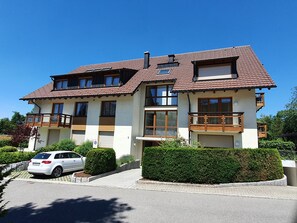 A two-story residential building with a tiled roof, multiple windows, balconies, and a parked car in the driveway. - Apartment 'Nr 1c' with Private Terrace and Wi-Fi (Titisee-Neustadt)
