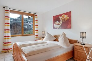 A bedroom with a wooden bed, two bedside tables, a window with curtains, and a wall-mounted painting. - Apartment 'Nr 1c' with Private Terrace and Wi-Fi (Titisee-Neustadt)