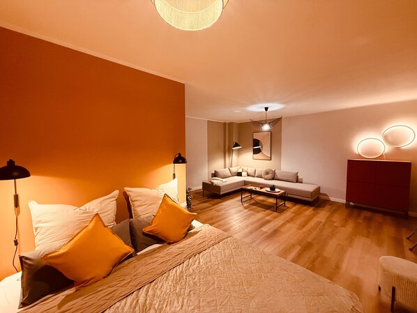 A modern hotel room with a bed, a sofa, a coffee table, and a red cabinet.