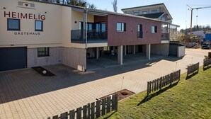 Een modern gebouw met de aanduiding 'HEIMELIG GÄSTEHAUS', een overdekt terras en een verharde binnentuin.