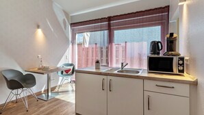 Een compacte keuken met een magnetron, spoelbak en een klein eethoekje met twee stoelen.