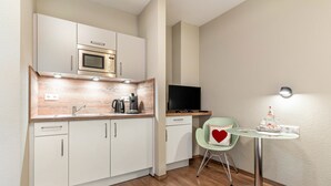 A compact kitchen with a microwave, coffee maker, and a TV. There's a small table with a chair and a heart-shaped pillow. - Studio 'Rebstock' with Wi-Fi (Herbolzheim)
