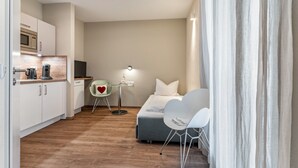 A compact hotel room with a kitchenette, a bed, a desk with a chair, and a window with curtains. - Studio 'Rebstock' with Wi-Fi (Herbolzheim)