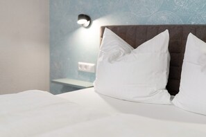 A neatly made bed with white bedding and pillows, a headboard, and a wall-mounted light fixture.