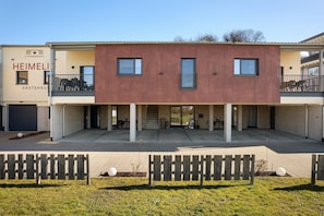 Un bâtiment moderne doté d’un toit plat, de deux balcons apparents et d’une enseigne indiquant « HEIMELI GÄSTEHAUS ».