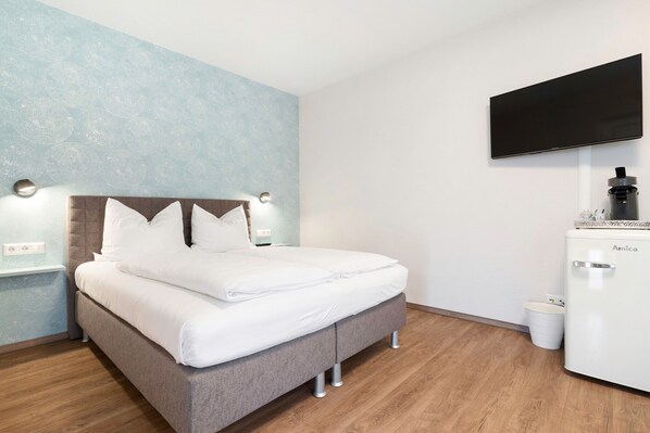 A neatly made bed with white linens, a grey headboard, and a flat-screen TV mounted on the wall.