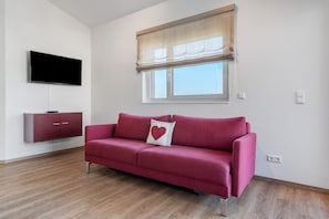 A room with a red sofa, a flat-screen TV, a wooden cabinet, and a window with a blind.