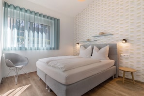 Une chambre à coucher avec un lit, une chaise, une table de chevet et une fenêtre avec des rideaux.