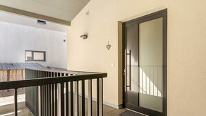 Exterior de um edifício moderno com porta de vidro, guarda-corpo de metal e uma pequena janela.