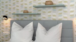 Quarto com cabeceira estofada cinza, almofadas brancas e duas prateleiras suspensas azul claro com cestos trançados.
