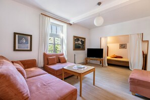 Een woonkamer met een bank, een salontafel, een televisie en een bed met gordijnen.