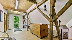 Amplia habitación en el ático con vigas de madera, un cofre de madera, un cuadro enmarcado y vistas por una puerta.